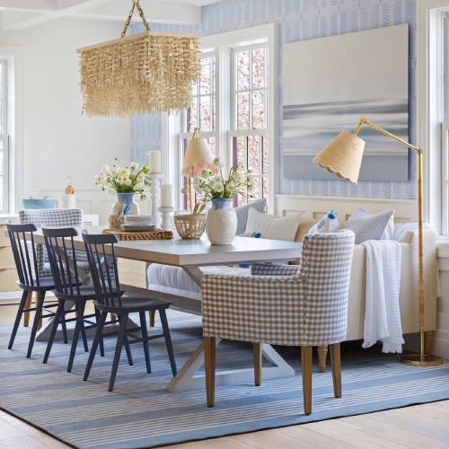 Coastal-inspired dining room with a blue rug, patterned chairs, and woven pendant light